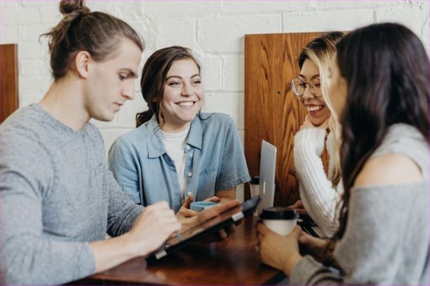 Four young people talking and laughing around a wooden table